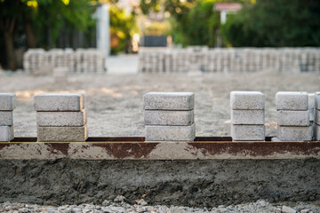 A construction area shows neatly stacked concrete blocks aligned along a metal edge, with gravel spread across the ground in preparation for paving work.