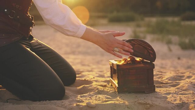 person body part close-up hands open treasure chest gold coins glowing shiny in sun light. Fantasy woman pirate finds treasure wooden box old style full of rich jewelry. Nature sand desert island 4k