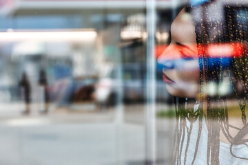 Young woman with braids looking through a window with city refle
