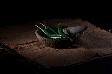 large green chilies in a stone mortar, prepared to be ground into a spicy chili sauce, photographed against a dark background