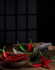 Large red and green chilies are ready to be ground in a stone mortar and pestle, mixed with shallots and garlic to make a spicy chili sauce which is characterized by the presence of thin smoke