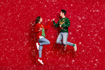 Full length portrait of two excited delighted people jumping raise fists success isolated on red color background