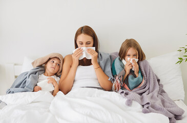 Portrait of young sick family of mother and two little children lying in bed covered in blankets...