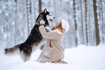 Cheerful woman in the snow playing with a husky dog. Friendship. Domestic dog concept.
