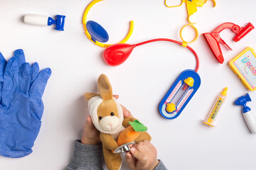Obraz premium Toy Doctor's Check-Up with Stuffed Animal and Medical Kit on White Background. Pretend Play Doctor Examining Stuffed Bunny with Blue-Gloved Hands.