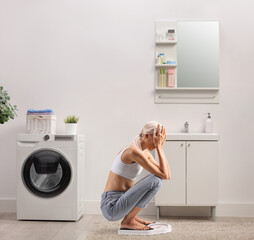 Worried young skinny woman kneeling on a weight scale