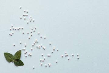 Homeopathic globules and mint leaves on blue background. Alternative medicine herbs, healthcare and pills concept. Top view. Copy space. Flat lay. Homeopathy