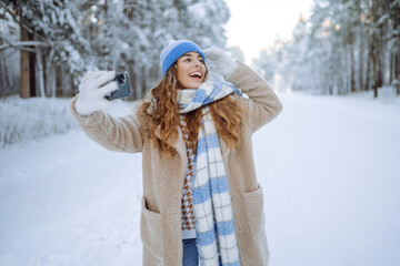 Smiling woman taking selfie and waving hand outdoors in winter park.  Concept of blogging, travel, weekend. Active lifestyle.