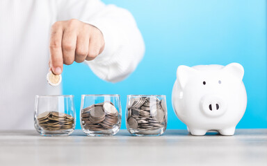 Man dropping coins into a glass jar, with a piggy bank nearby. Represents the concept of saving money, highlighting the importance of building a financial cushion through various saving methods.