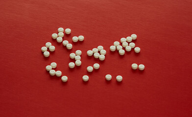 White pills scattered on a red background, careless attitude toward health, importance of medication for cardiovascular health, fragility of health, taking care of health.