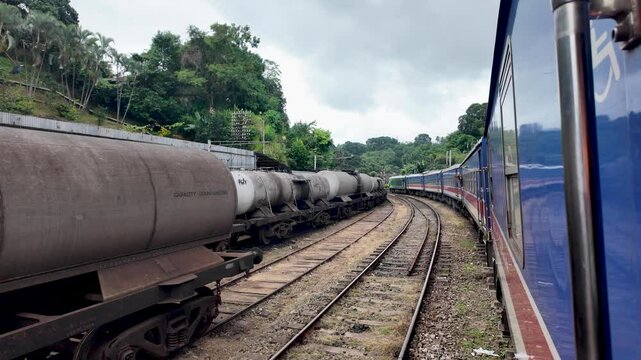 Stationary local train waits beside chemical freight tank trains on a railway track in Sri Lanka.
