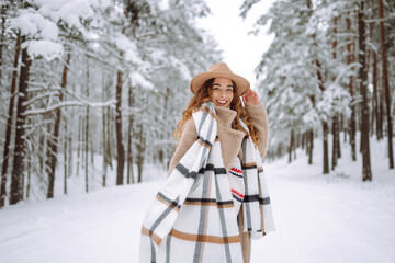 Happy woman among snowy trees in winter forest, enjoying the first snow in hat and coat. Boho style. Active lifestyle and tourism.