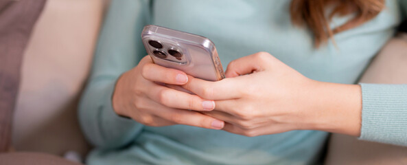 Closeup hand of happiness young asian woman sitting on sofa using smart phone with cozy in living room at home, happy woman on couch watching social media on smartphone with relax, lifestyles concept.