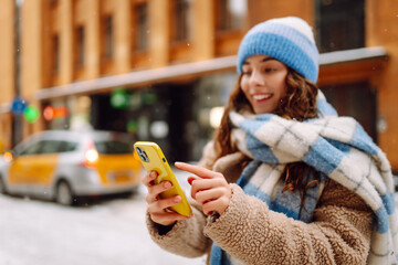 Phone in the hand of young woman in  winter street. Online communication. Technology concept.