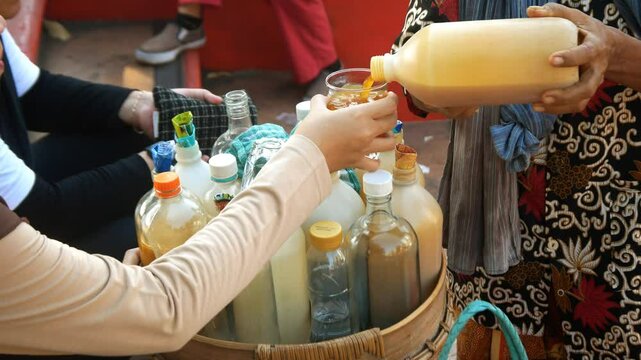 Seller's hand and bottle of jamu gendong, traditional Indonesian herbal drink, pouring the drink to serve the customer