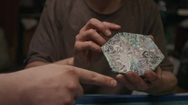 Close-up of hands of unrecognizable male technician or recycling workshop owner inspecting new sample of tile produced by extrusion from reclaimed polymer resin, testing for durability