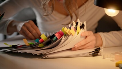 Workaholic woman at office desk sorting stack of paper documents with binder clips and puts...