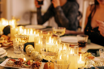 A covered festive table with New Year decor. Lighted candles, snacks, Christmas balls