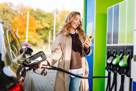 Beautiful woman filling her car with gasoline at the gas station. Online pay. Woman pays for a gas station using an app on her phone. - Powered by Adobe