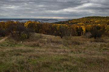 Fototapeta premium The hill overlooks the river, surrounded by yellow trees that seem to dip autumn into the water.