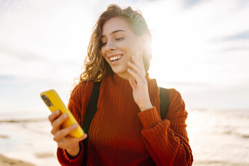 Young woman using mobile phone at beach. Cold weather. Autumn.  Blogging, communication, technology...