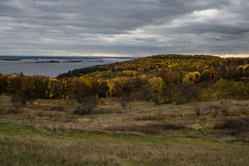 Fototapeta premium The hill overlooks the river, surrounded by yellow trees that seem to dip autumn into the water.