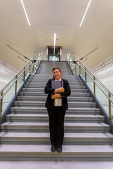 Smiling Young Businesswoman Holding Laptop in Front of Stairs at Modern Office Building