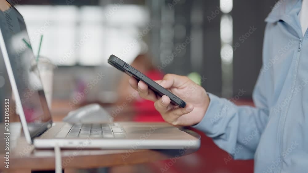Wall mural a man is holding a cell phone while sitting at a table with a laptop. the man is looking at the phon
