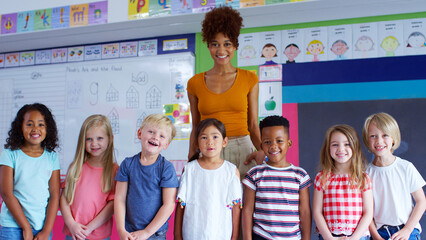 Portrait Of Multi-Cultural Elementary School Pupils Standing In Classroom With Female Teacher