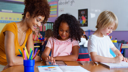 Elementary School Teacher And Female Pupil Drawing Using Digital Tablet In Classroom 