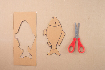 a piece of cardboard with a fish shape cut out of it, step in creative process, red handle...