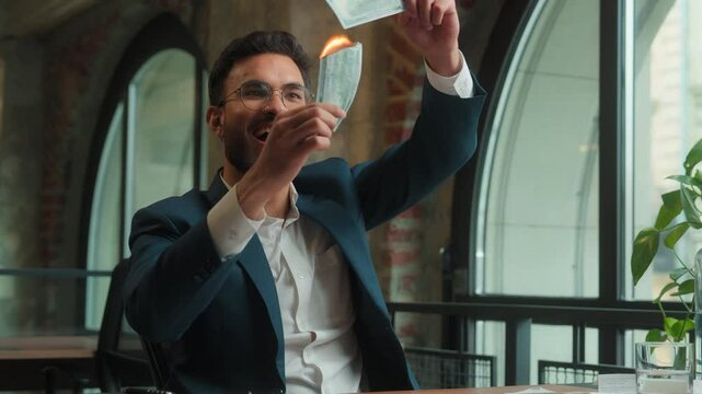 Indian Arabian male guy business man businessman crazy mad happy fooling laughing at office hold burning fake money trick joke waste cash enjoy burn paper banknotes finance excited rejoice have fun