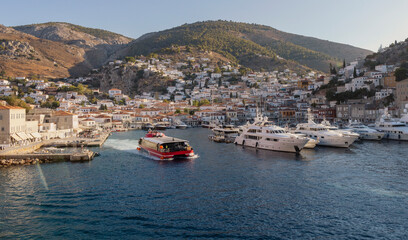 A colorful boat navigates the serene waters of Hydra's harbor, showcasing the town's charming architecture and the surrounding hills. The scene captures the essence of this beautiful Greek island.