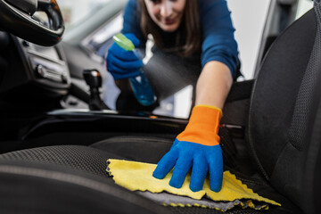 A woman cleans the interior of a car with a cloth in a detailed cleaning session in a well-lit...