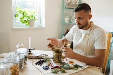 Man adds dried mint to a mortar and pestle. Homemade healthy and nutrition supplements