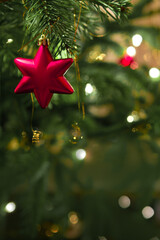 Red Christmas star hanging on fir tree against blurred festive lights.