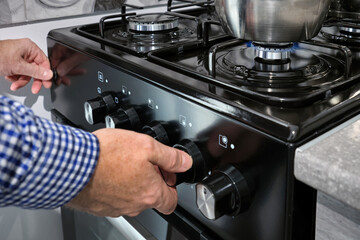 An elderly man turns on a gas stove to cook food.