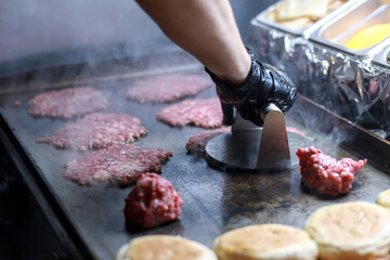 Unrecognizable person smashing raw smash burgers balls on a hot grill to make burgers in a restaurant kitchen