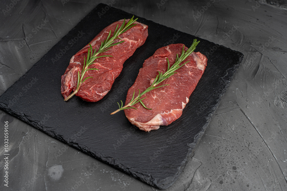 Wall mural two pieces of raw meat for steaks with a sprig of rosemary on a black mica board on a dark backgroun