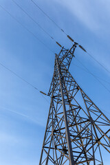 High voltage transmission tower stands tall against expansive clear blue sky above. Low angle shot.