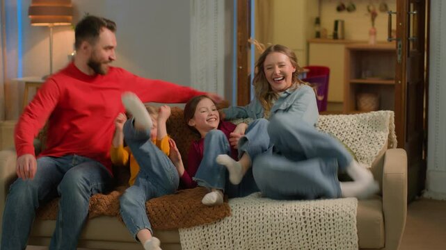 Happy Caucasian family little kids girls siblings daughters mother father gather together home evening weekend funny carefree children parents mom dad jumping on couch sofa bonding have fun moving day