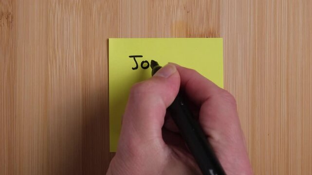 A person is writing on a sticky note on a wooden background. The person is writing John 3:16. Concept, religion, Christianity, Bible verse.
