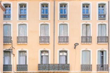 Facade of a colonial building with symmetrical windows and iron balconies in the French town of Perpignan.