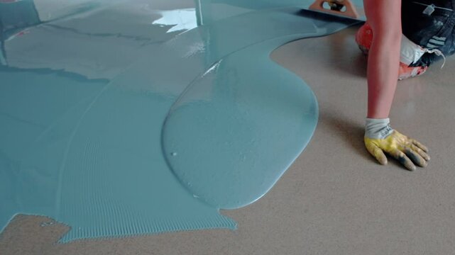Construction worker spreading blue epoxy resin on floor
