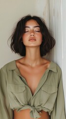 Fototapeta premium Young woman exudes calm, leaning against a wall with eyes closed, showcasing natural beauty in a stylish green shirt