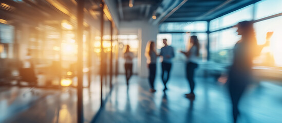 Blurred image of colleagues interacting in a modern office environment at sunset, creating a soft, warm, and dynamic atmosphere, emphasizing teamwork and collaboration
