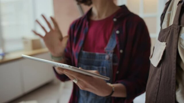Cropped shot of anonymous female home owner with digital tablet talking about her ideas of room interior design to repairman during redecoration process
