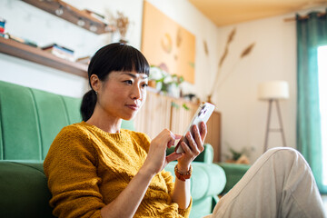 Smiling Asian woman using smartphone at home