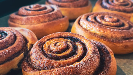 Delicious cinnamon rolls on baking paper, side view. Background of freshly baked cinnamon rolls. Close-up of homemade sweet pastries made from yeast dough