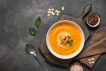 Pumpkin cream soup with croutons on wooden cutting board, dark grunge background, top view, winter and autumn warming soup